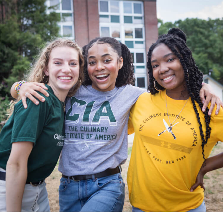 Three smiling CIA students attending culinary school in New York.