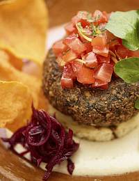 A gourmet burger patty topped with diced tomatoes and herbs, accompanied by a side of crispy vegetable chips and a small portion of shredded purple cabbage, all artistically arranged on a plate.