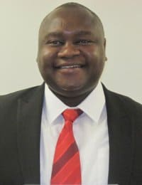 A person in a suit jacket, white shirt, and red tie is smiling in this portrait image. The background is plain and white.