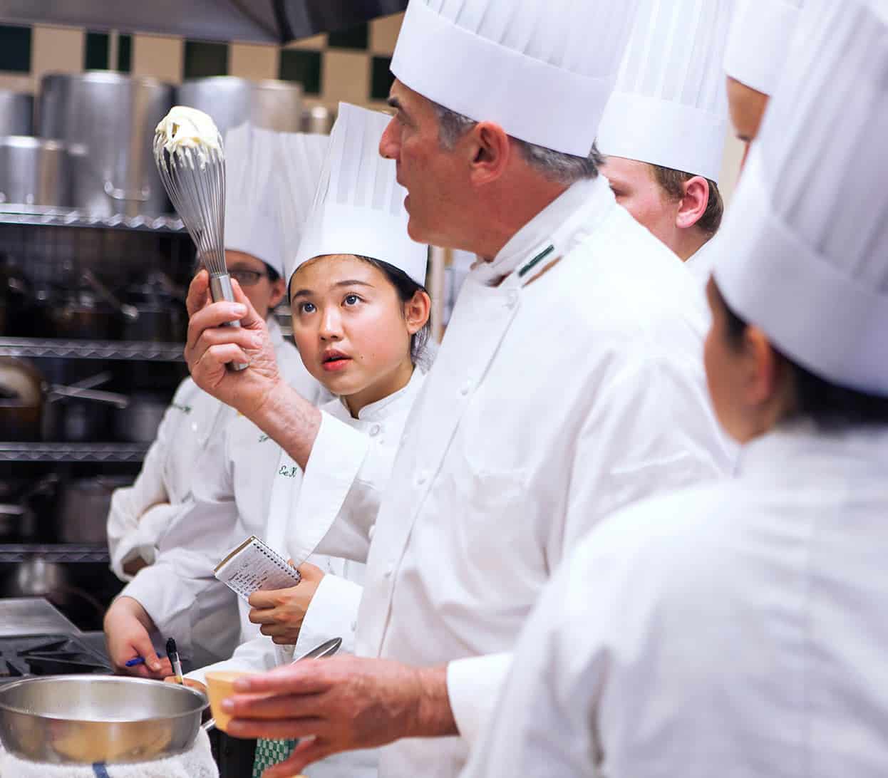 CIA students working on fundamentals with a chef in the kitchen.