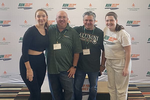 Four people in front of CIA’s step and repeat at the 13th annual Run for Your Knives 5K held during Alumni Weekend on the Hyde Park, NY campus.