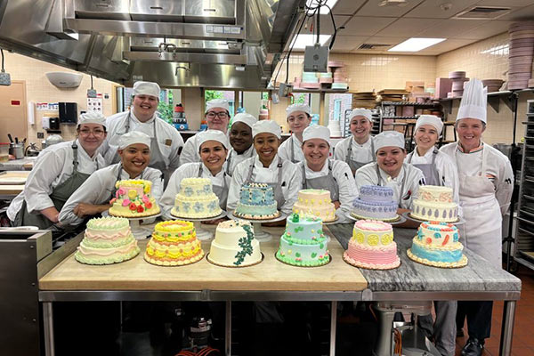 Image of smiling students standing behind the cakes they created in their baking and pastry arts class.