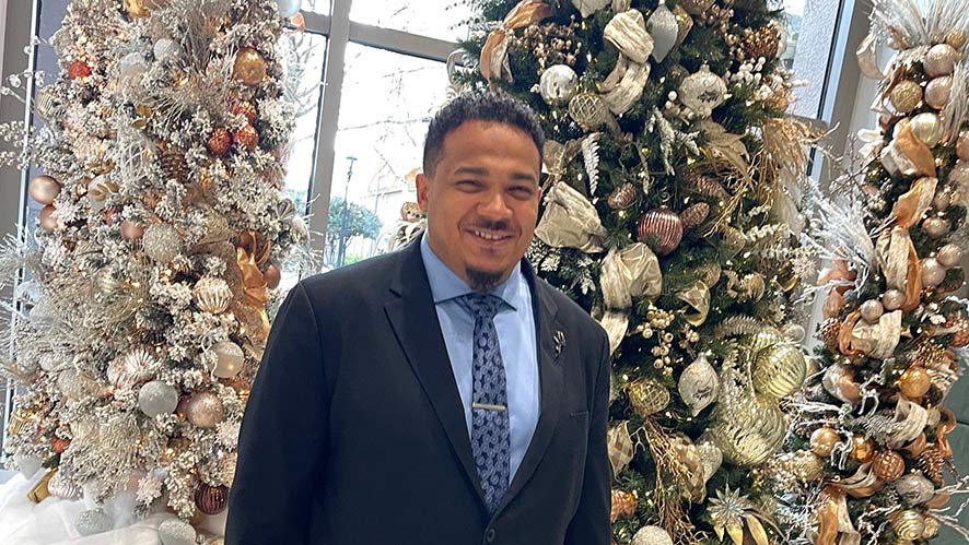 A smiling Eric Jones in a suit stands in front of decorated Christmas trees.